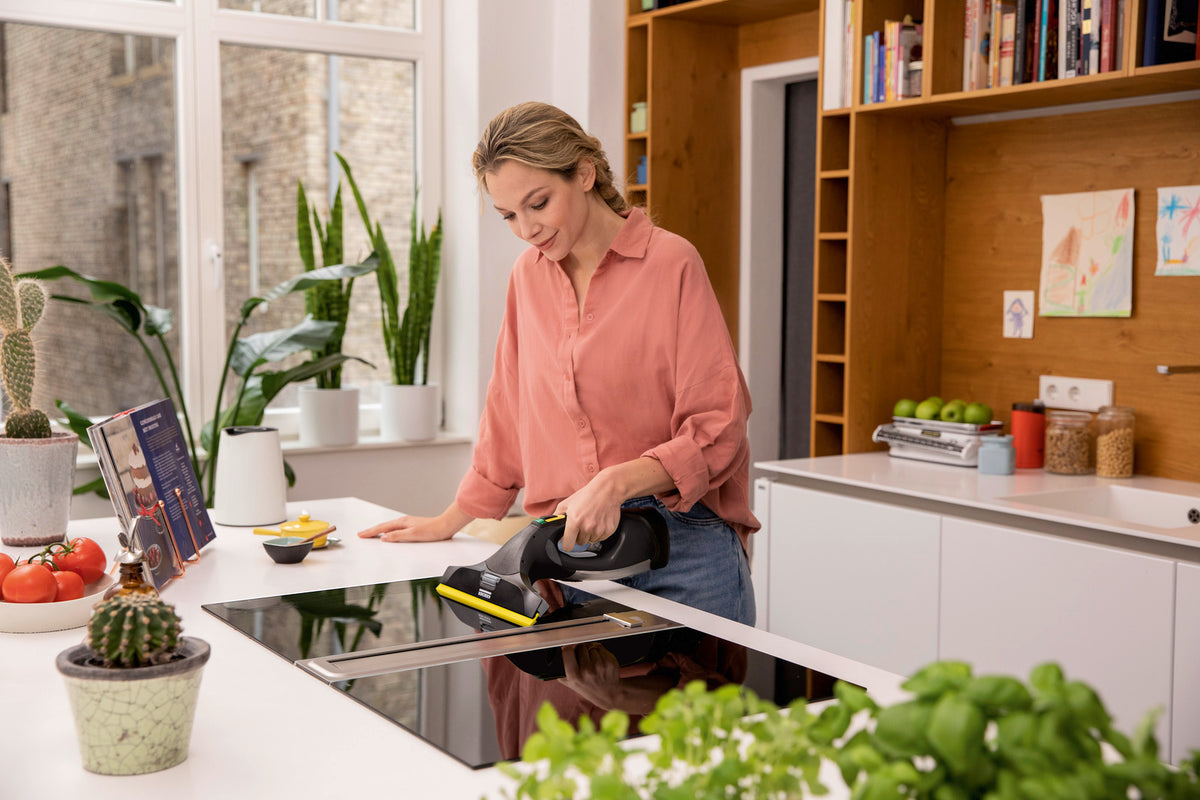 Woman using Karcher WV5 Anniversary Window Vac to clean a kitchen stovetop in a bright modern kitchen.
