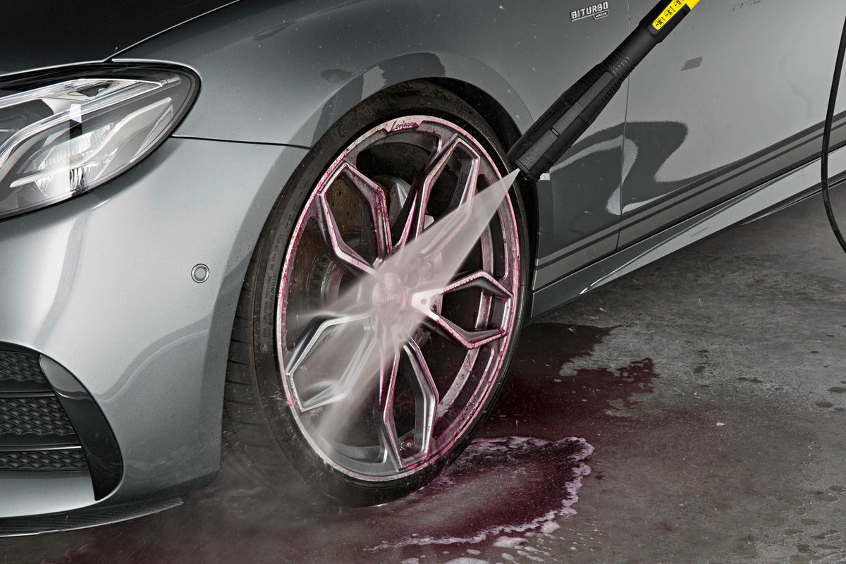 Silver car wheel being cleaned with Karcher Rim Cleaner, showing purple cleaning foam and water spray.
