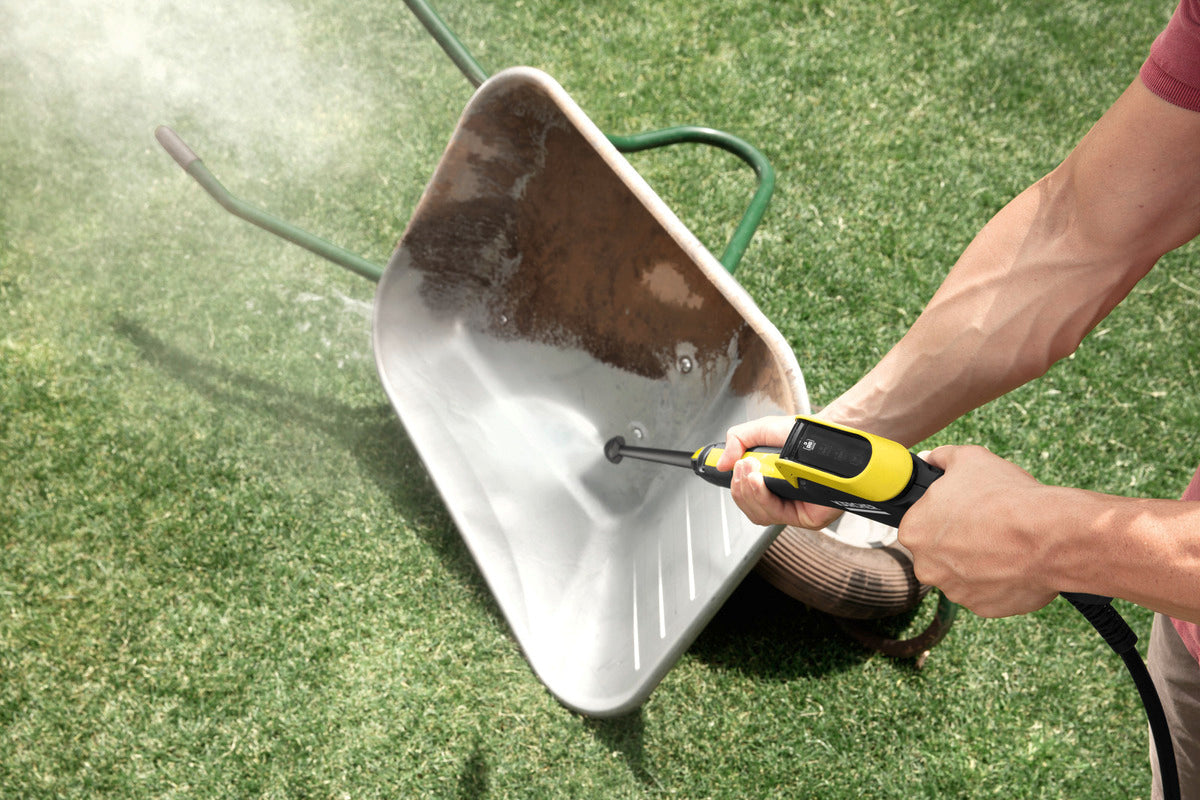 Person using Karcher Full Control Dirt Blaster DB145 to clean dirt from a metal wheelbarrow on grass