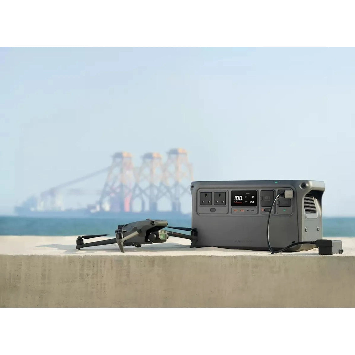 DJI Power 1000 portable power station with digital display and outlets, connected to a drone on a concrete ledge.
