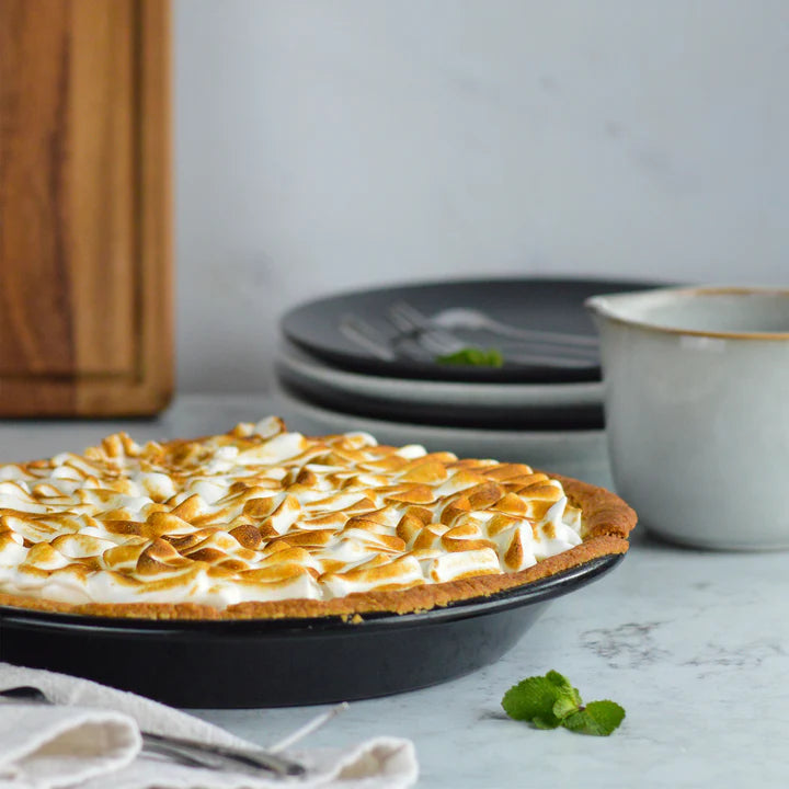 Tala Eclipse 9" black pie dish holding a toasted meringue pie on a marble surface with plates and cup nearby