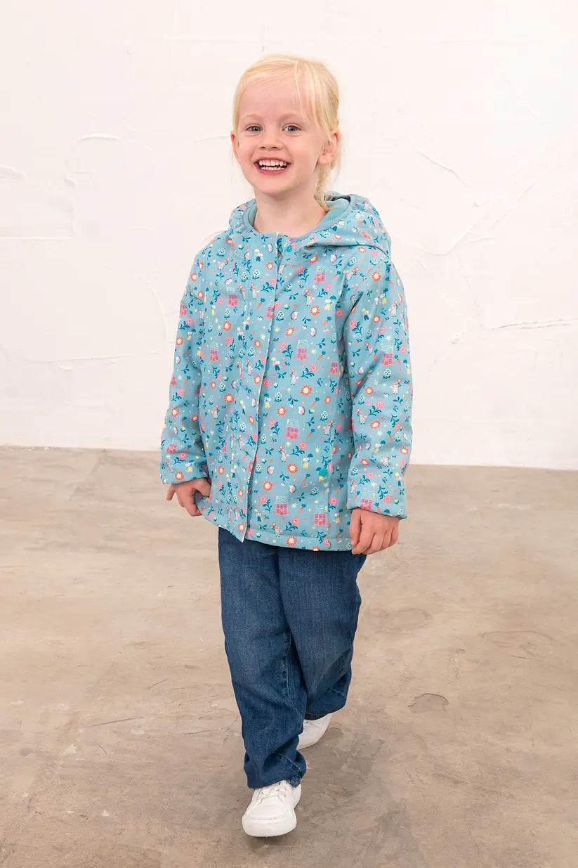 Smiling girl wearing a blue Freya Girls Waterproof Coat with floral print, jeans, and white sneakers.