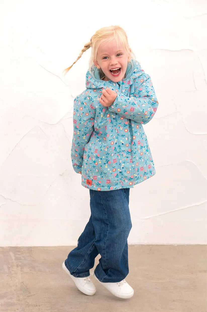 Young girl wearing a blue Freya Girls Waterproof Coat with floral and cottage print, smiling and jumping.