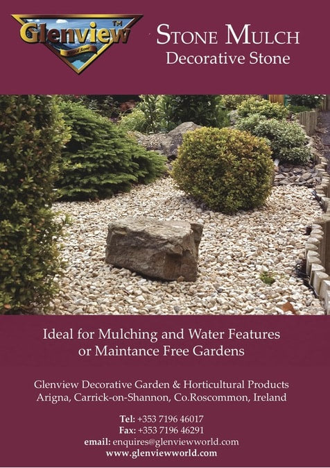 Decorative light-colored stone mulch spread in a garden bed with shrubs and a large rock centerpiece.