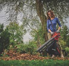 Woman using Einhell Power X-Change 18V VENTURRO cordless leaf blower/vac to collect leaves outdoors.