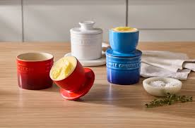 Le Creuset Butter Crocks in cerise and blue, with butter inside, displayed on a wooden table.