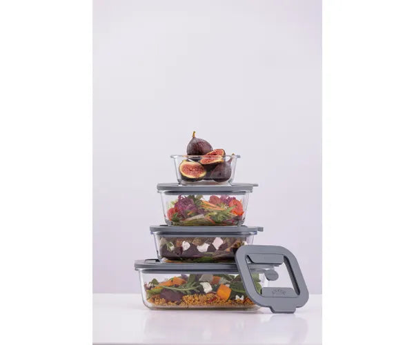 Stack of four rectangular glass storage containers with grey lids, filled with various foods, one lid off to the side.