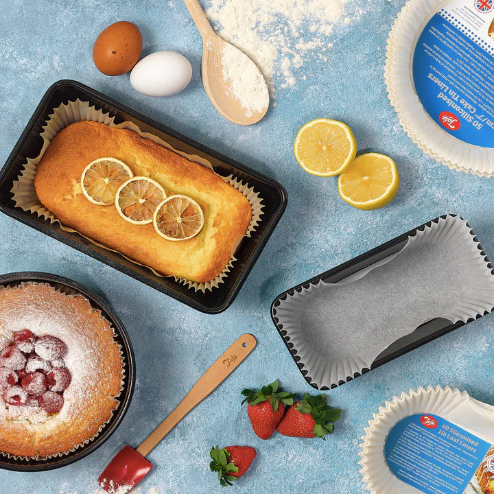 Tala 50 siliconised 18cm cake tin liners in use with baked cakes, eggs, flour, lemon, and strawberries on blue surface.