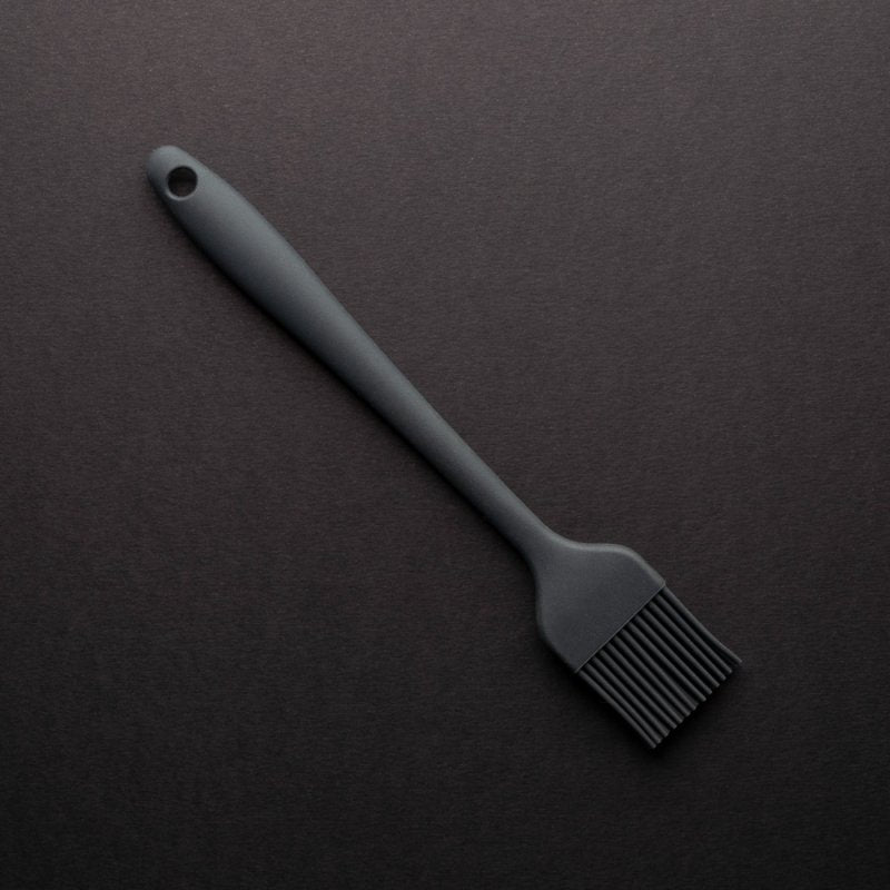 Graphite silicone pastry brush with long handle on a dark background, angled top left to bottom right.