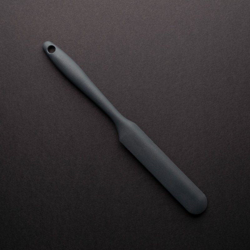Graphite-colored mini palette knife with a smooth handle and rounded blade on a dark background
