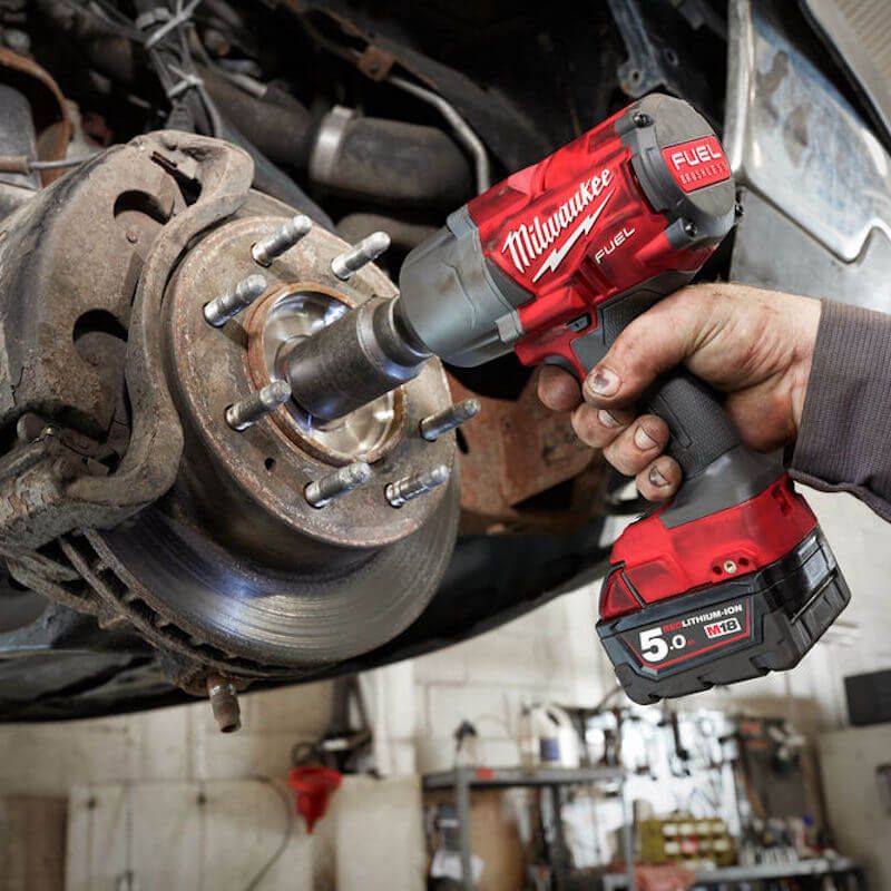 Hand holding Milwaukee M18 Fuel High Torque Impact Wrench removing lug nuts from a vehicle brake rotor.