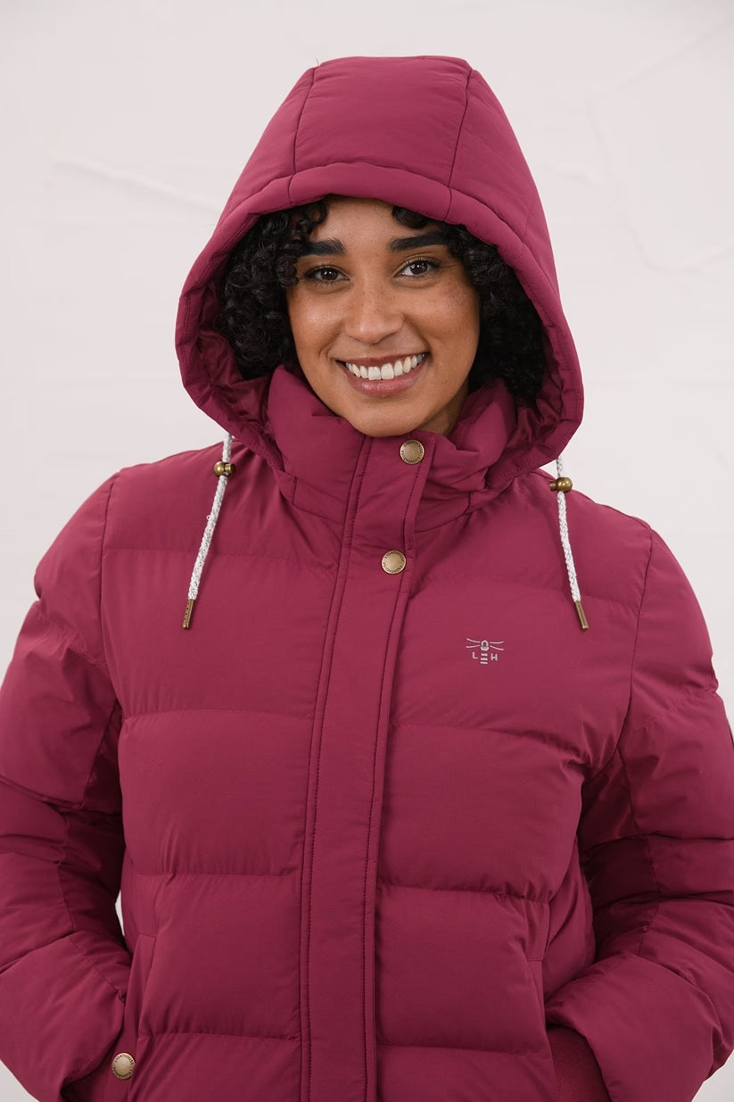 Woman wearing a berry-colored Margot Ladies Coat with hood up and hands in pockets, smiling at camera.
