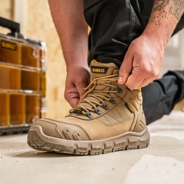 DeWalt Milburn Stone Waterproof Boot in tan, shown being laced up on a concrete floor.