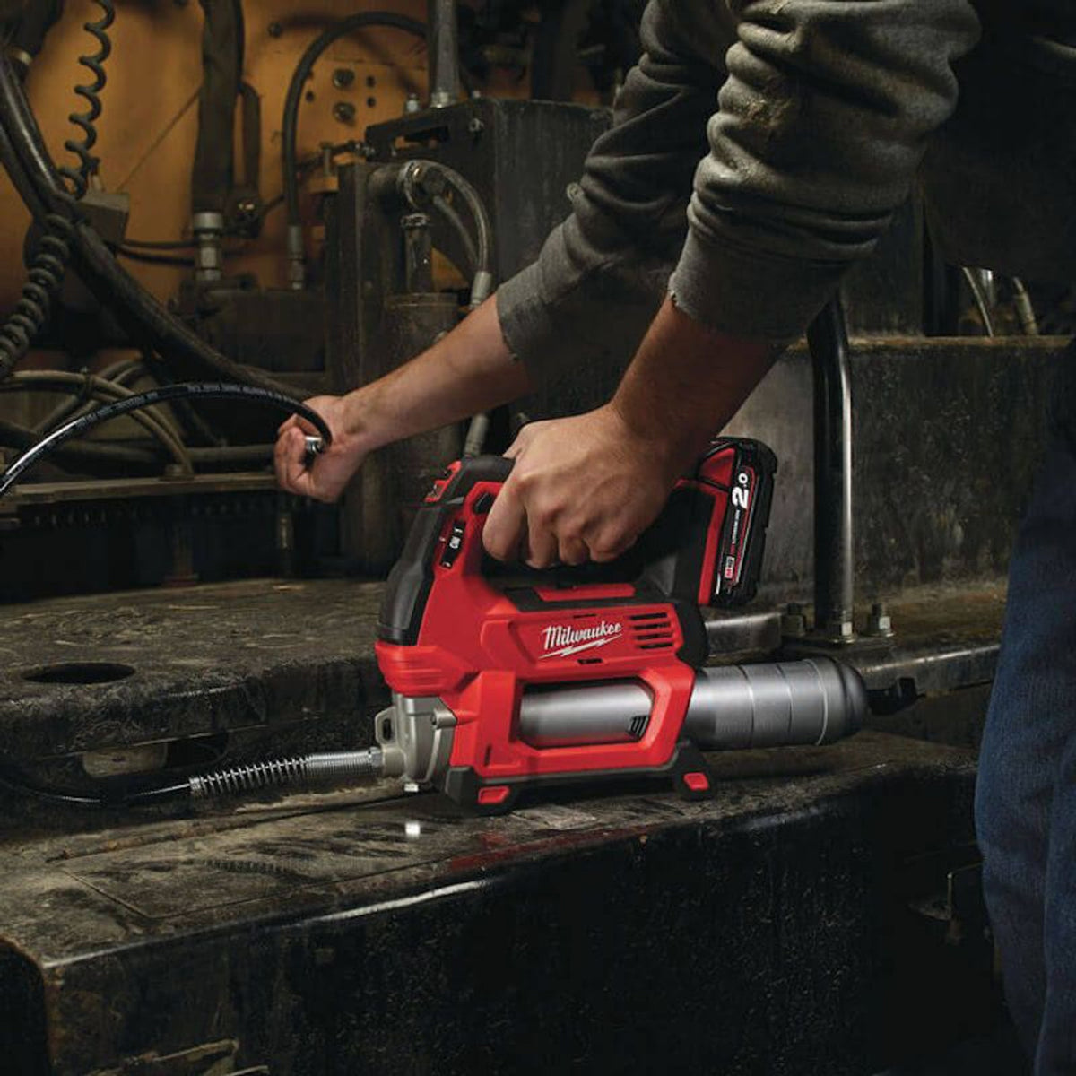 Hands using a red Milwaukee M18 Fuel cordless grease gun on industrial machinery.