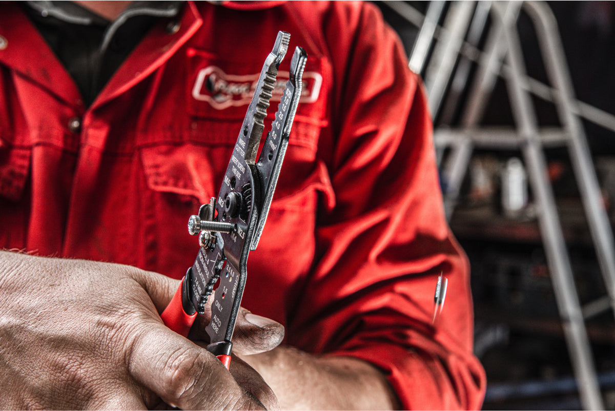 Close-up of Milwaukee multi-purpose wire stripper with crimper held by person in red workwear