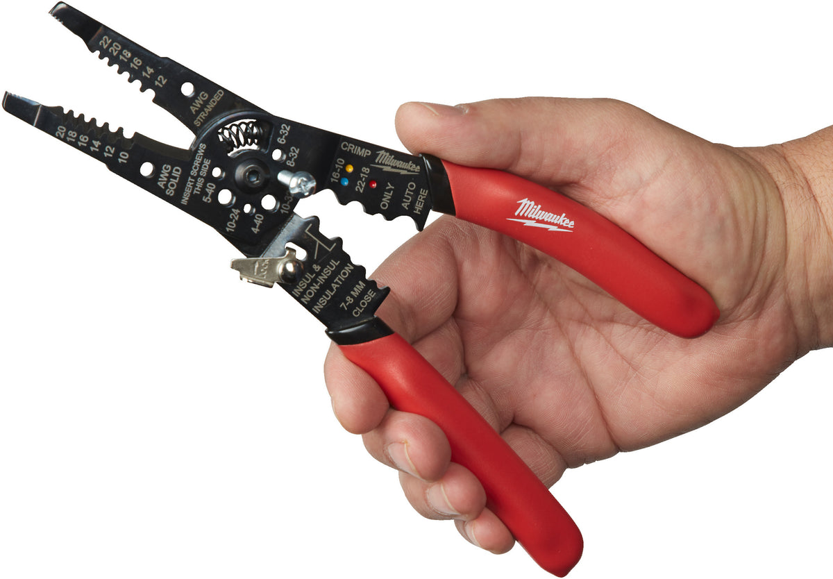 Hand holding Milwaukee multi-purpose wire stripper with red handles and black metal stripping and crimping head.