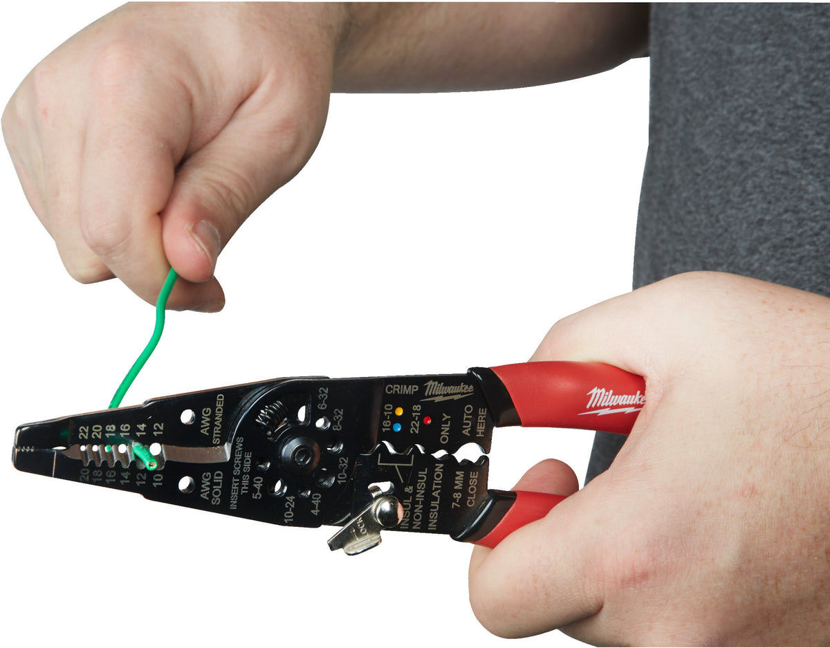 Hands using Milwaukee Multi-Purpose Wire Stripper with Crimper to strip green wire insulation.