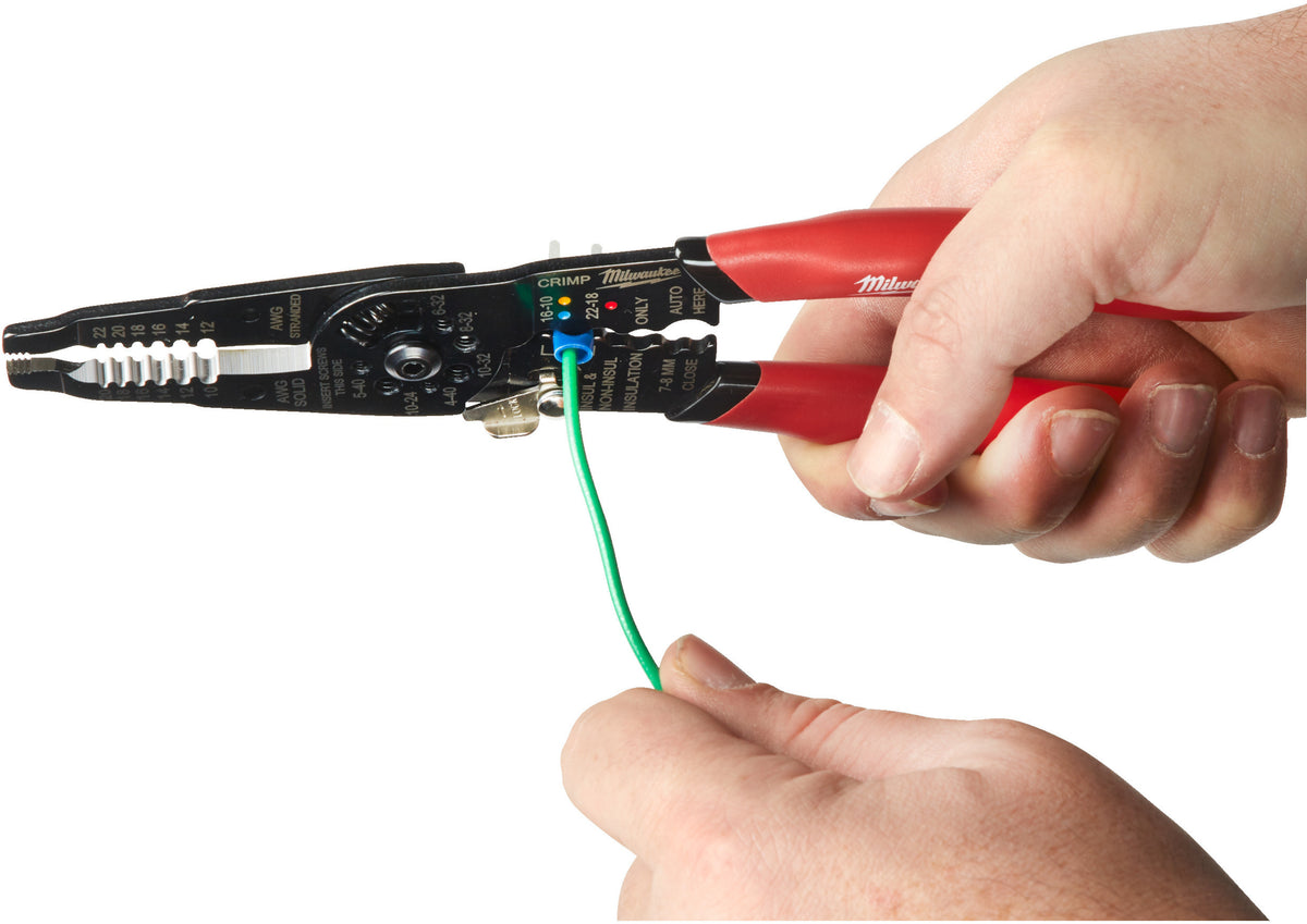 Hand holding Milwaukee multi-purpose wire stripper with crimper stripping green insulated wire on white background.