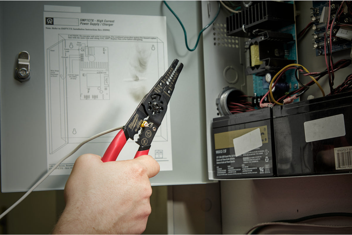 Hand holding Milwaukee Multi-Purpose Wire Stripper with Crimper near electrical panel wiring.