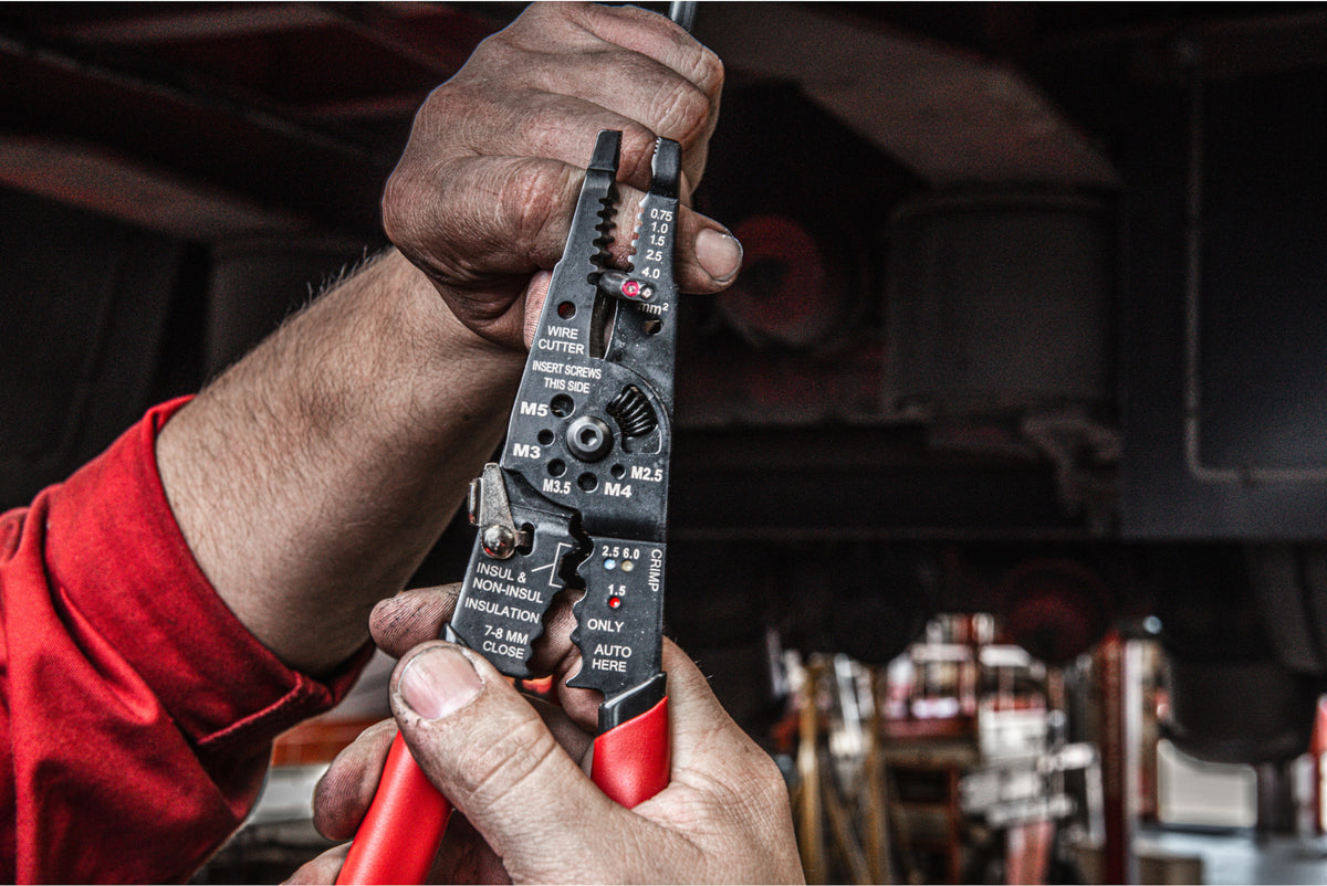 Hands holding a Milwaukee multi-purpose wire stripper with red handles and visible wire gauge markings.