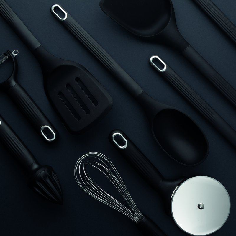Black silicone solid spoon among various black kitchen utensils on a dark background