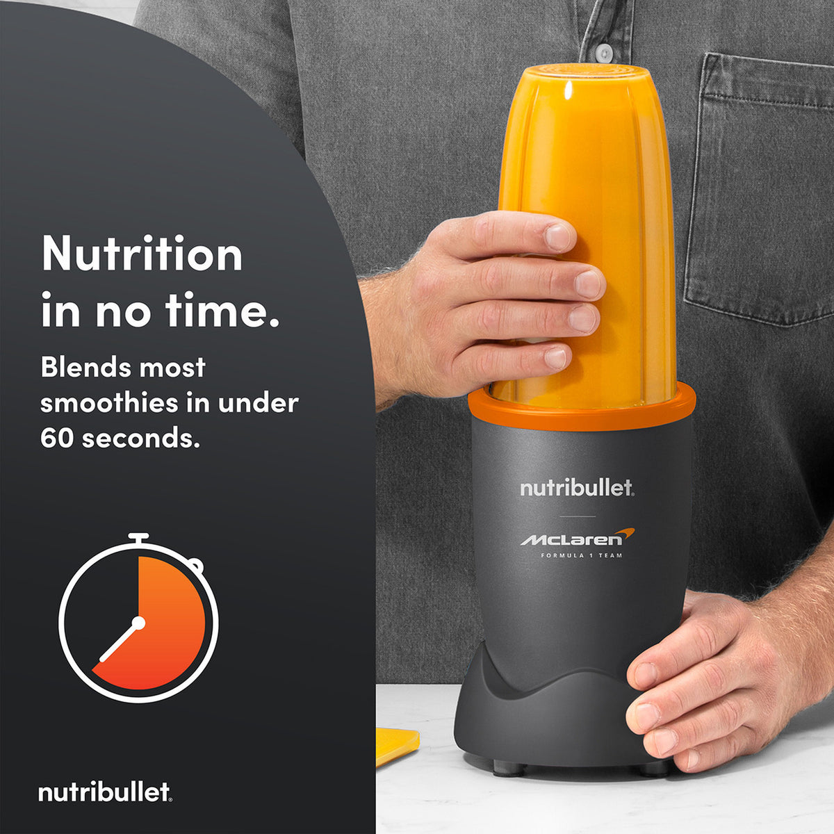 Hands holding a Nutribullet 900 McLaren blender with orange smoothie cup on a white surface