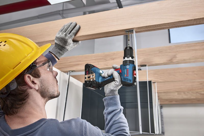 Man wearing a yellow hard hat using Bosch 18V Combi Drill to screw metal bracket into wooden beam.
