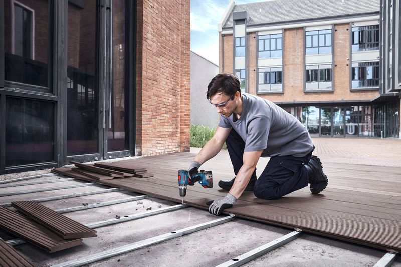 Man using Bosch 18V Combi Drill to install decking boards on an outdoor patio.
