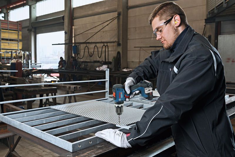 Man using Bosch 18V Combi Drill to drill into metal sheet in industrial workshop setting