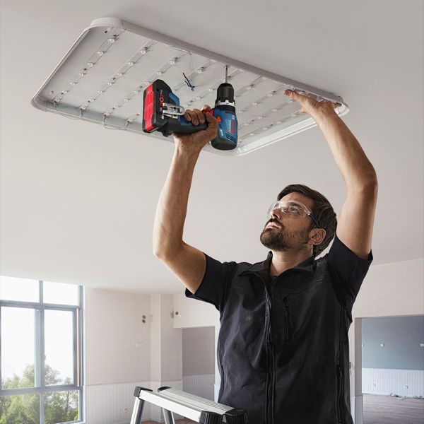 Man using Bosch 18V Combi Drill to install a ceiling light panel, wearing safety glasses.