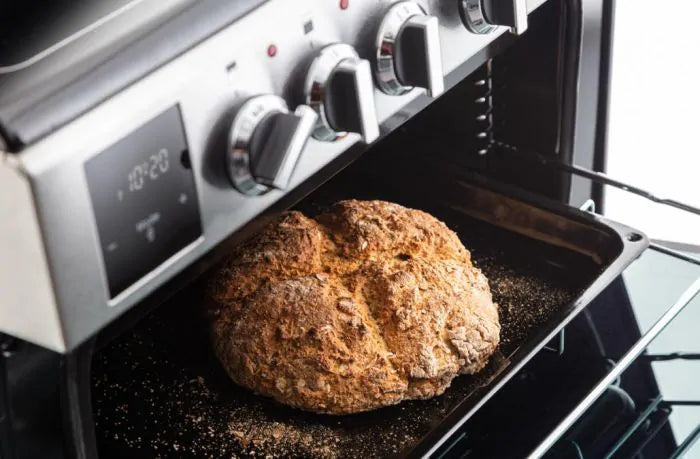 Rangemaster PROPL60ECSS/C stainless steel ceramic cooker with oven door open, baking bread on tray.