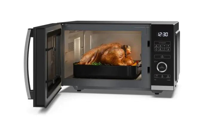 Sharp 25L 900W silver flatbed microwave with open door showing a roasted chicken inside on a black tray.
