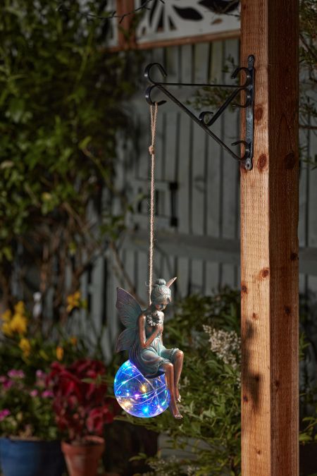 Solar Fairy Fantasy statue sitting on a glowing, multicolored light orb, hanging from a wooden post outdoors at dusk.