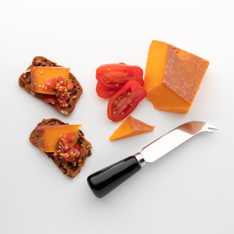 4 Piece Ceramic Cheese Set with black handle knife next to cheddar cheese, tomato slices, and crackers with cheese topping