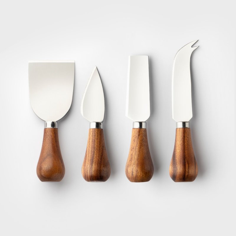 Four acacia-handled cheese knives with stainless steel blades arranged side by side on white background