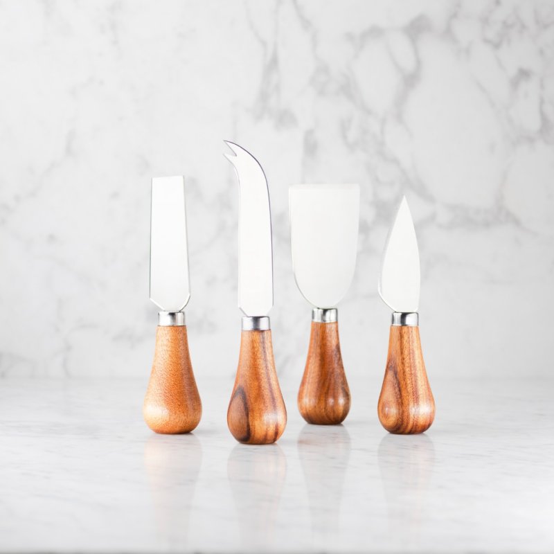 Four acacia-handled cheese knives with stainless steel blades standing upright on a marble surface.