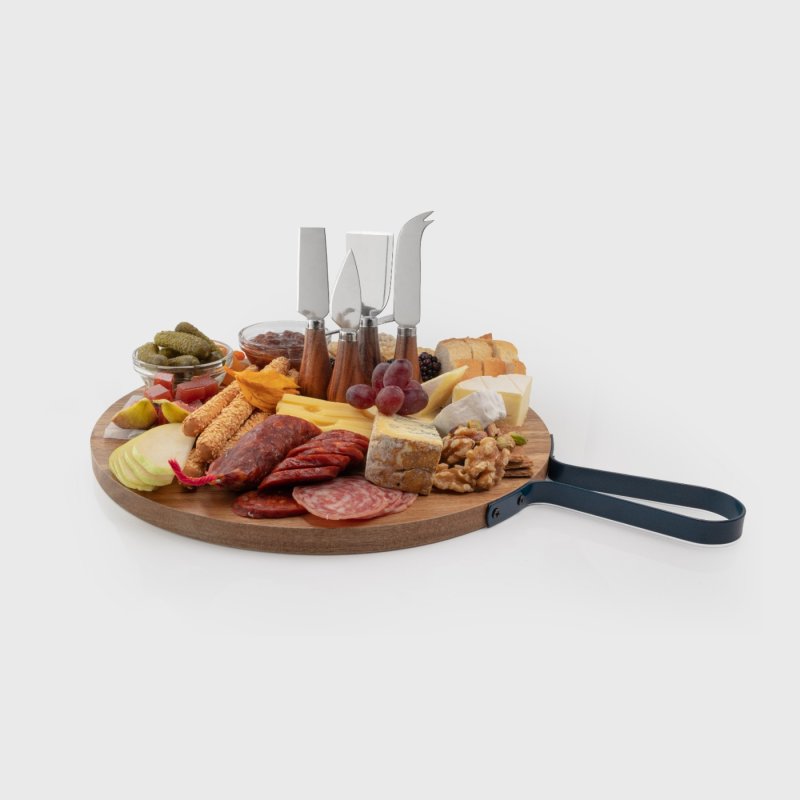 Round acacia wood charcuterie board with four cheese knives and assorted meats, cheeses, nuts, and fruits.
