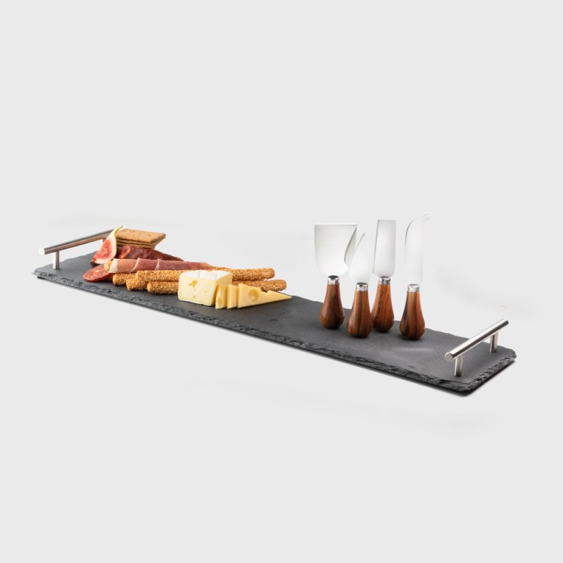 Slate charcuterie board with metal handles, four acacia cheese knives, cheese, crackers, and cured meats.