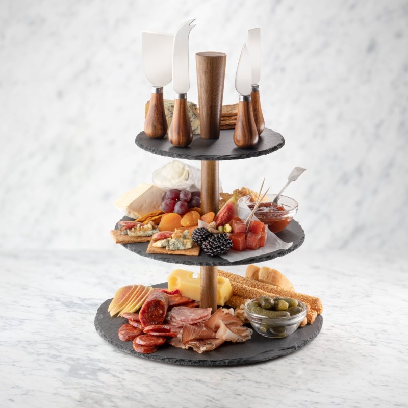 Three-tier slate étagère with assorted cheeses, meats, fruits, crackers, and four acacia-handled cheese knives on top.