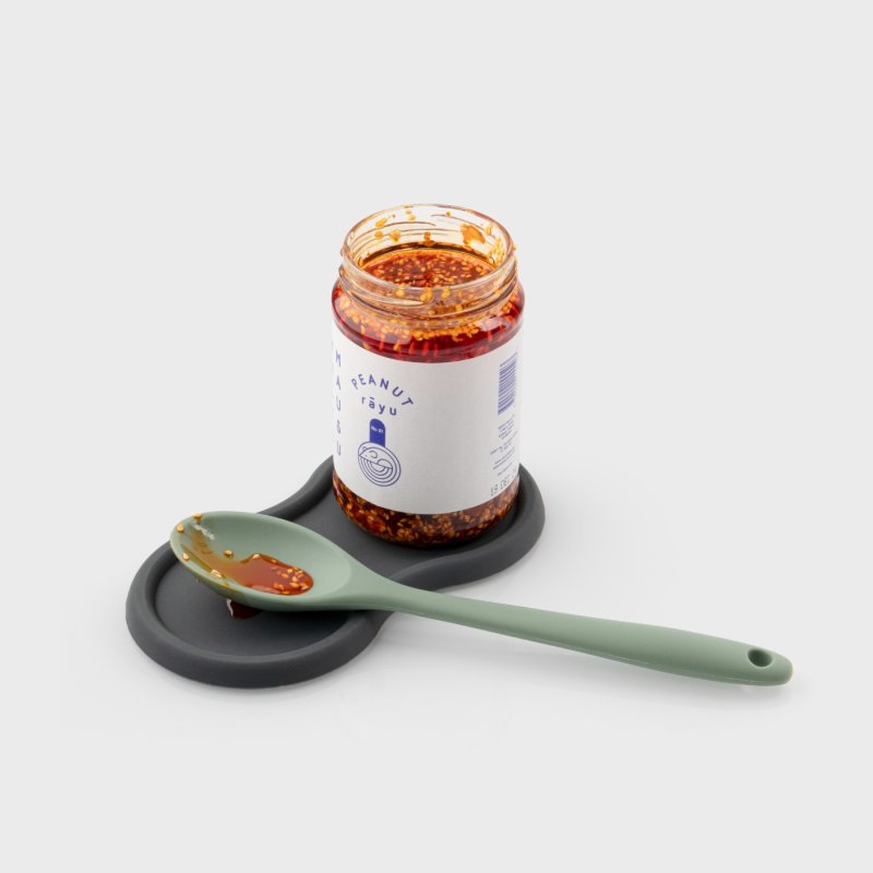 Graphite silicone mill and bottle stand holding a jar and a green spoon with chili oil on it.
