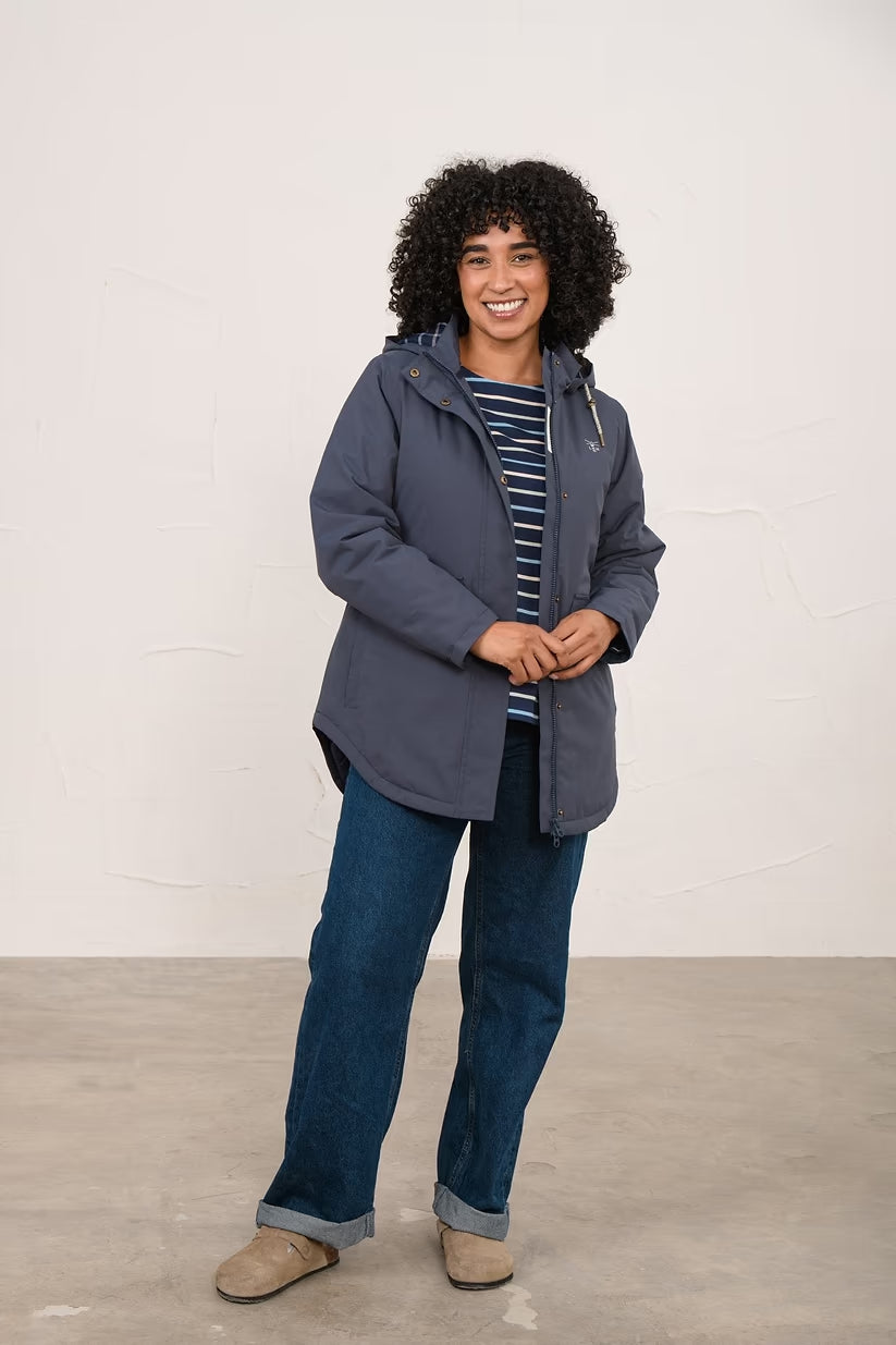Woman wearing a navy Tess Ladies Waterproof Coat with hood, paired with striped top and jeans, smiling.