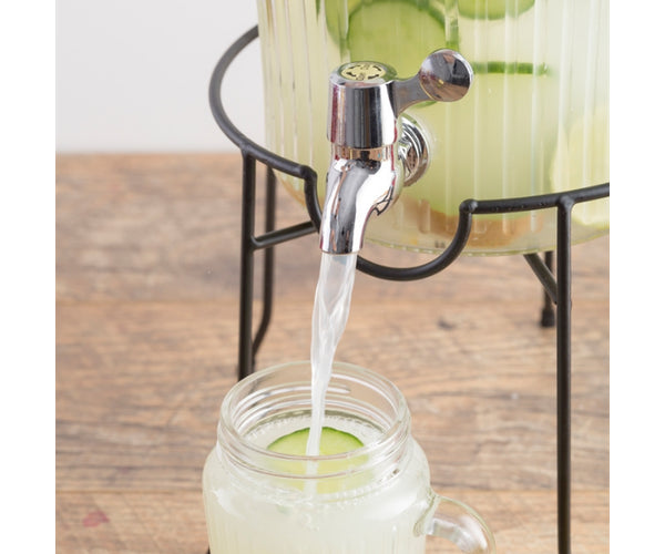 Close-up of Kilner drinks dispenser tap pouring liquid into a glass jar with cucumber slice.
