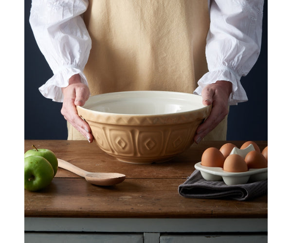 Person holding a beige Cane S18 Mixing Bowl 26cm with embossed diamond pattern on wooden table with eggs and apples