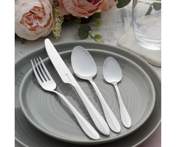 Four polished stainless steel cutlery pieces—a fork, knife, tablespoon, and teaspoon—on a gray plate.