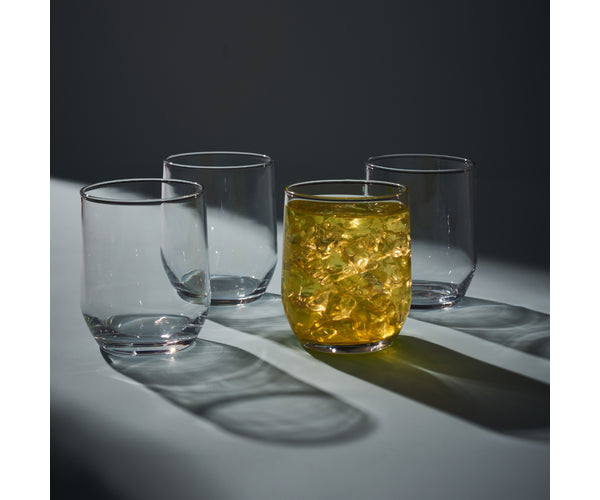 Set of four clear Ravenhead Tulip mixer glasses, one filled with a yellow drink and ice, casting shadows.