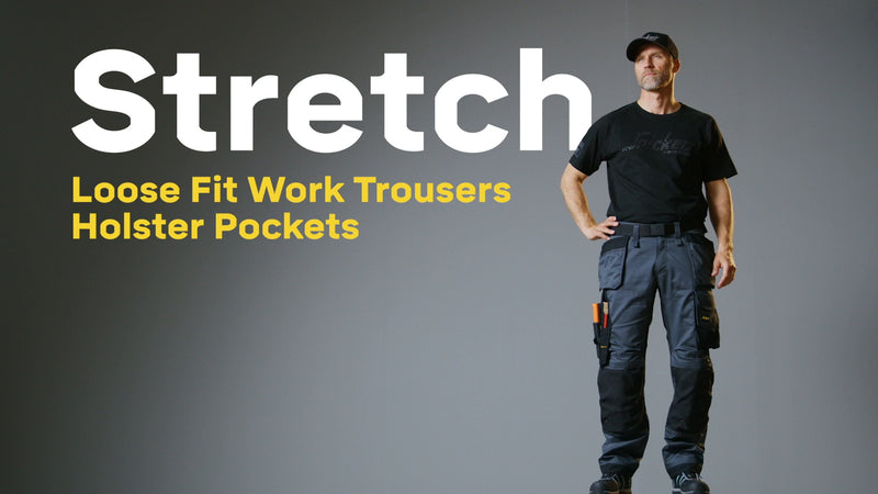 Man wearing navy and black Snickers 6251 stretch loose fit work trousers with holster pockets, standing against gray