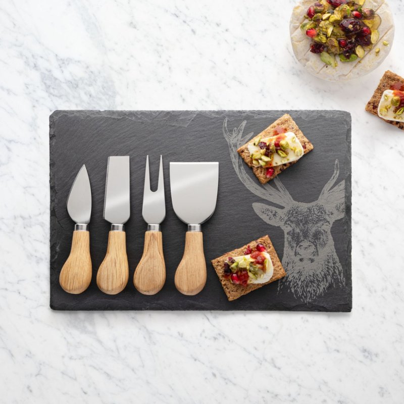 4-piece oak handle cheese knife set on a stag-engraved slate board with crackers topped with cheese and nuts